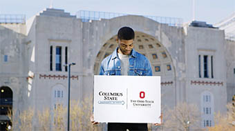 哥伦布州立大学的学生在俄亥俄州立大学的马蹄铁体育场前举着优先路径标志(哥伦布州立大学到俄亥俄州立大学)。